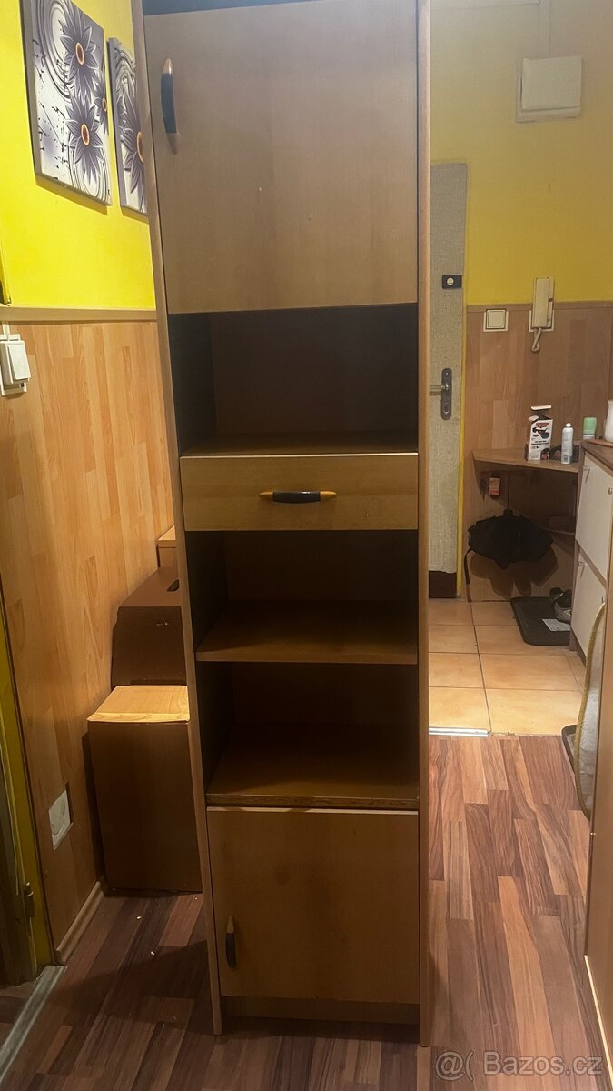 Úzka  dřevěná skříňka se zásuvkou a policemi.