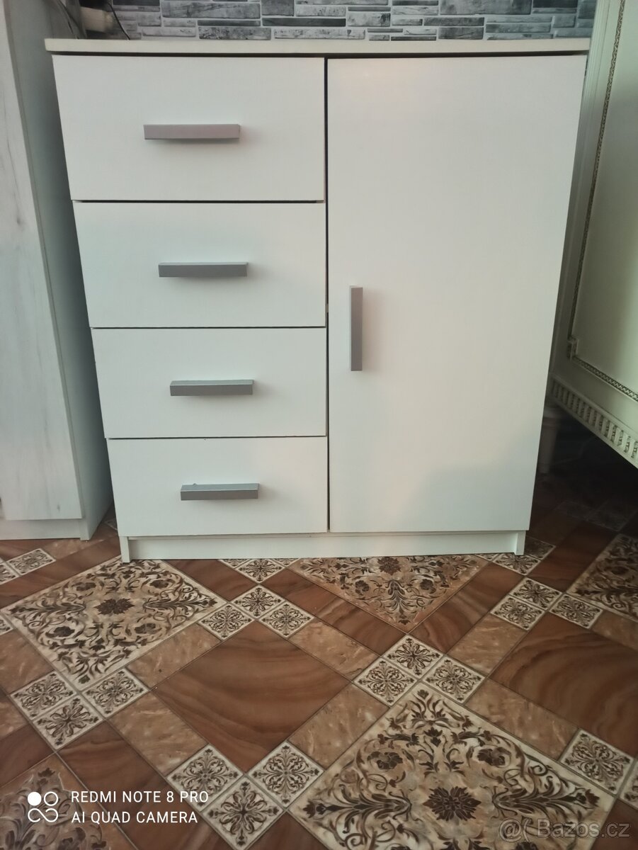 Bílá komoda se stříbrnými úchytky.