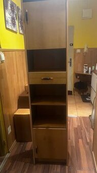 Úzka  dřevěná skříňka se zásuvkou a policemi.